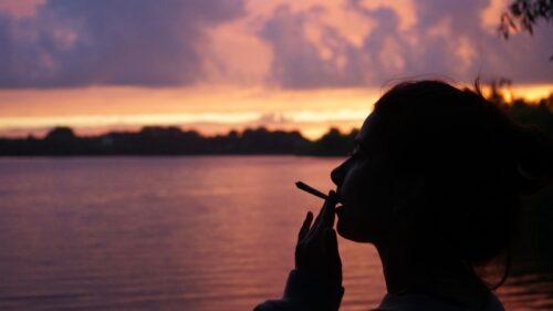 A woman smoking a cigarette in front of a body of water, FDA approves cannabis study for PTSD, FDA cannabis study for PTSD in veterans